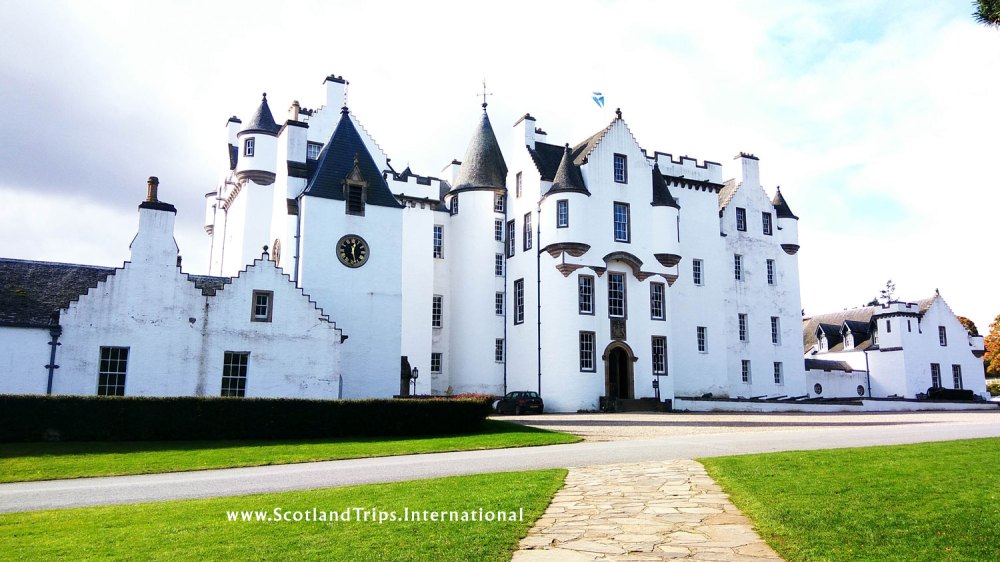 White historic castle with turrets and a courtyard under a partly cloudy sky.