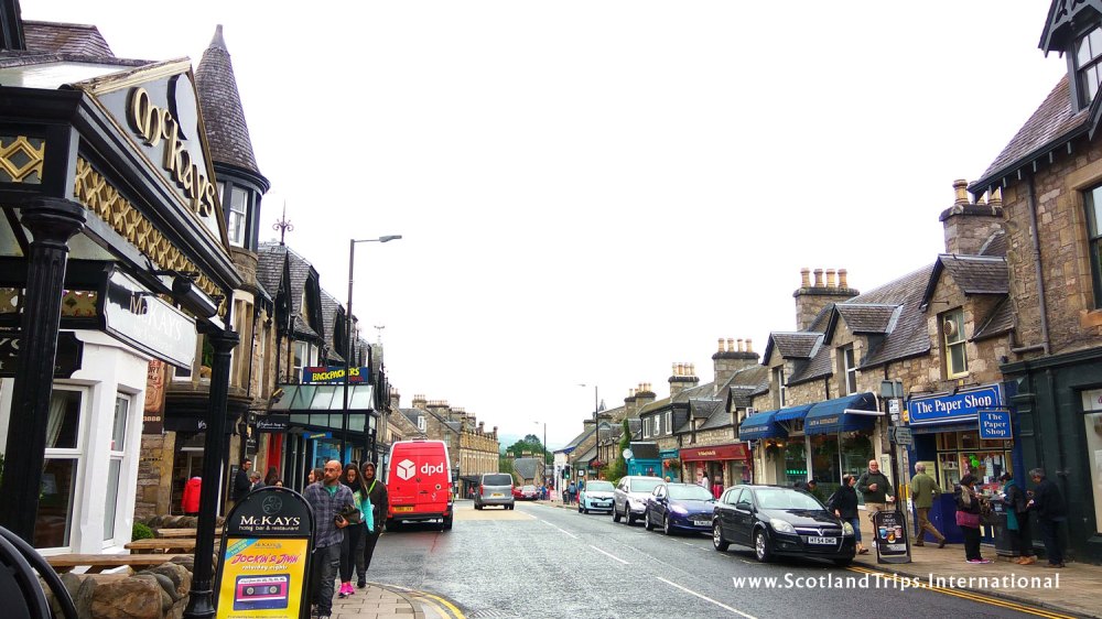 Street view of a quaint town with shops and cars parked along the road.