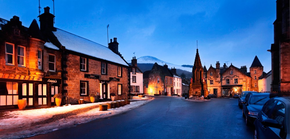 Quaint village square at dusk with stone buildings and snow on the ground.