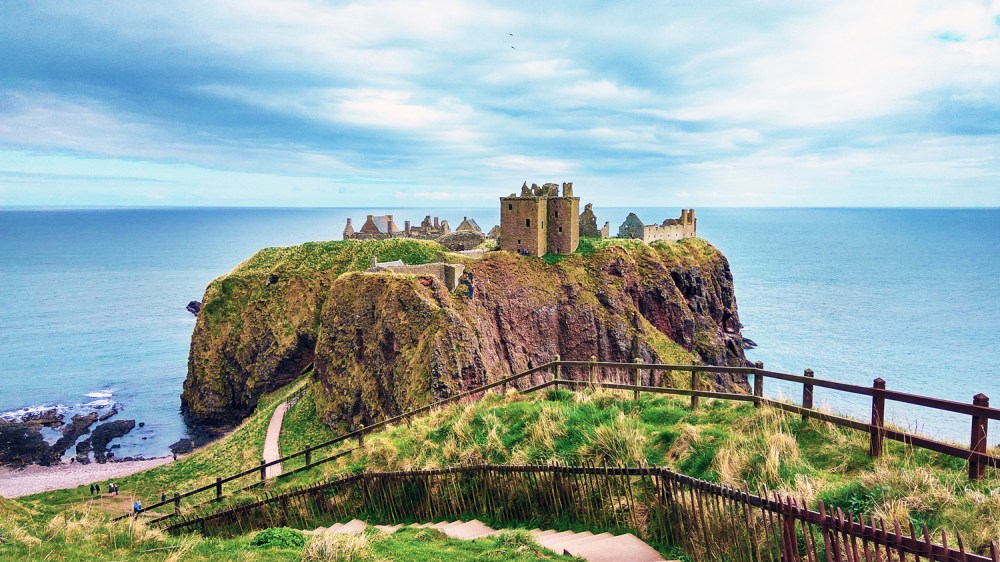 Ancient stone castle on a grassy cliff overlooking the sea.
