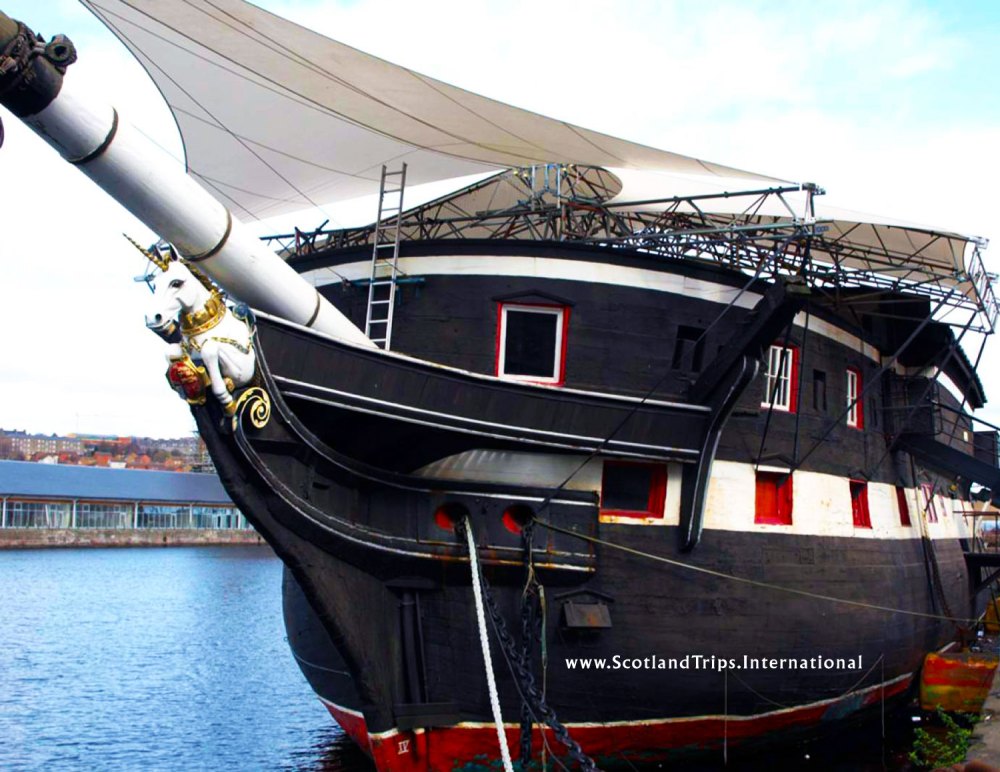 Historic black sailing ship docked at a harbor.