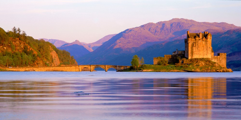 Medieval castle by a calm lake with mountains in the background.