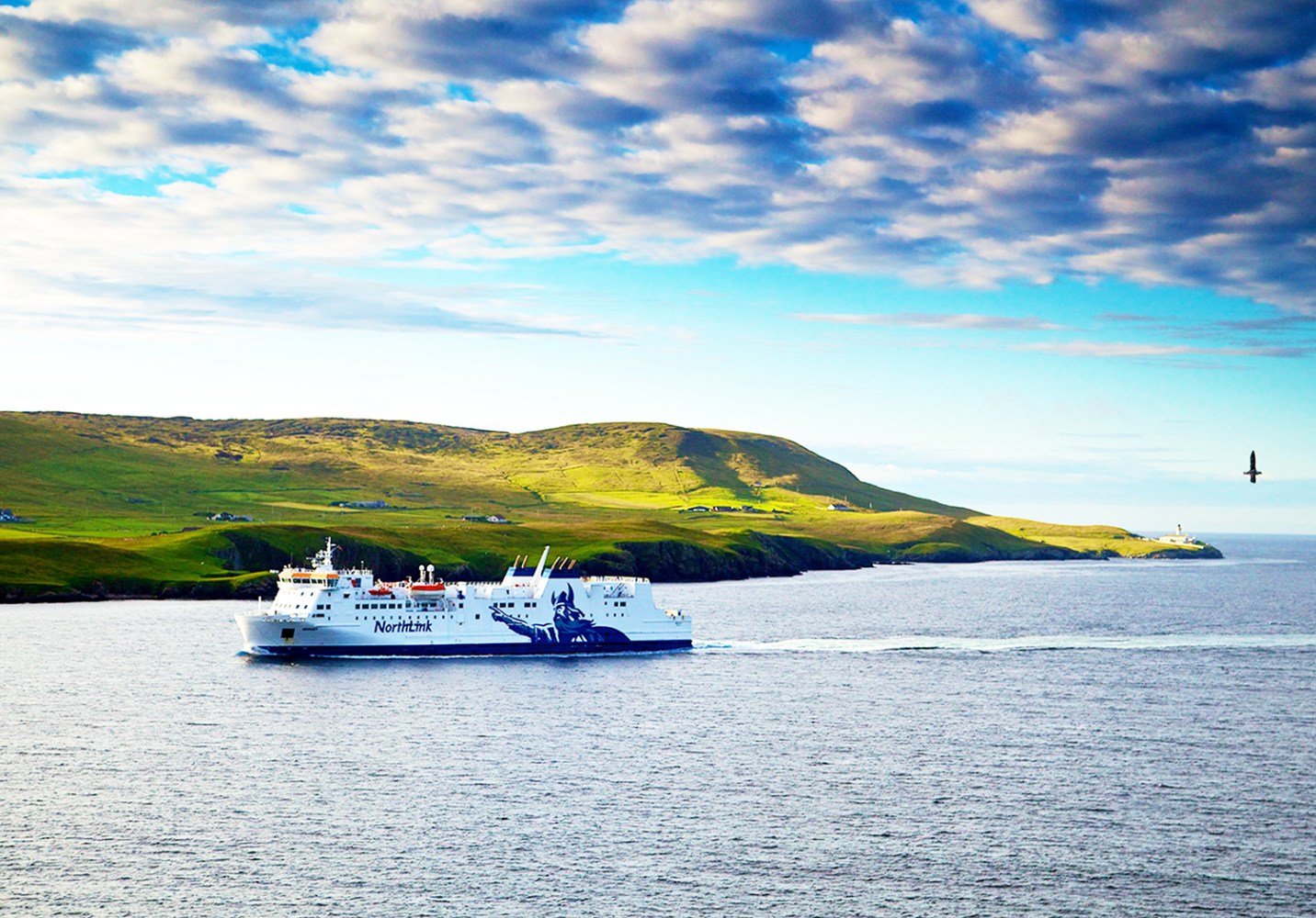 Ferry sailing near a green hillside under a partly cloudy sky.