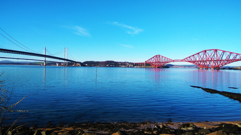 Two bridges over a calm blue river under a clear sky.