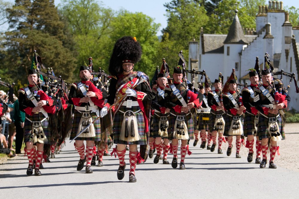 Bagpipe band in tartan kilts marching outdoors.