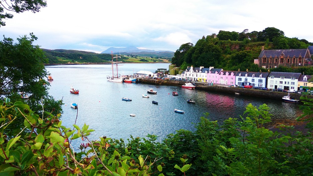 Scenic harbor view with colorful buildings, boats, and lush greenery.