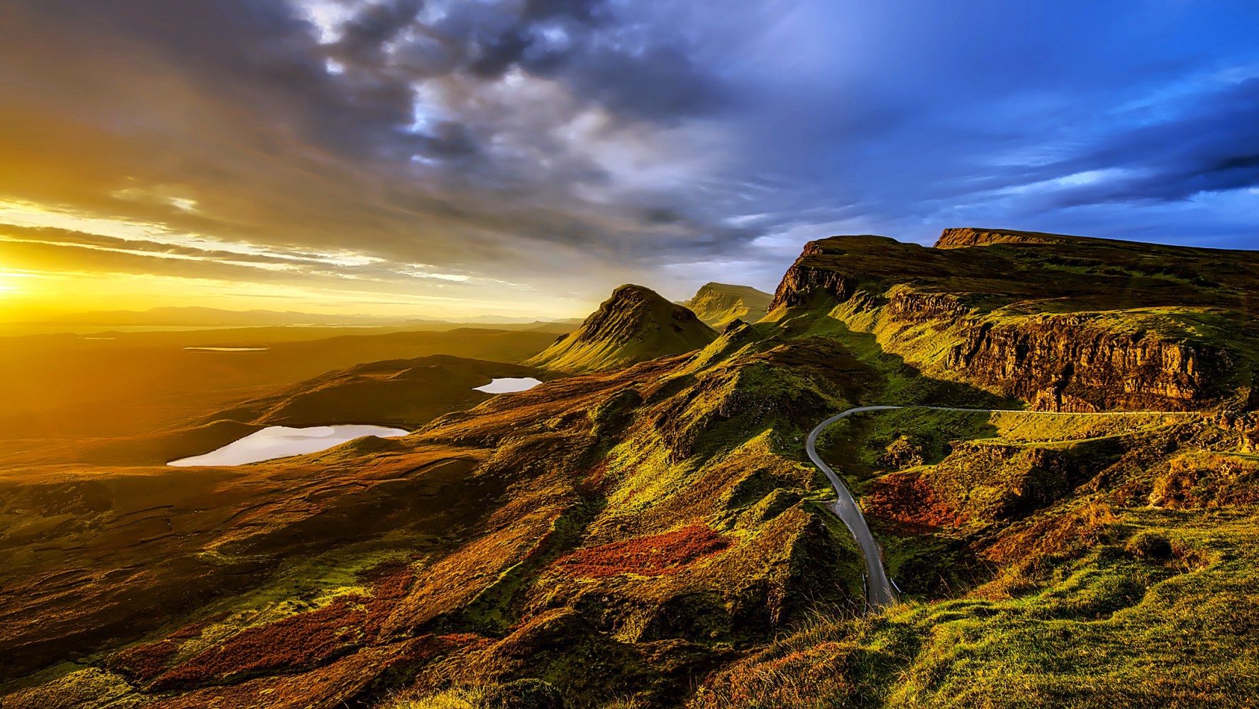 Scenic view of mountains at sunrise with a winding road and a lake.