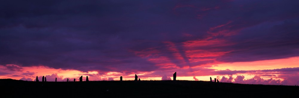 Silhouetted standing stones against a vibrant purple and pink sunset sky.