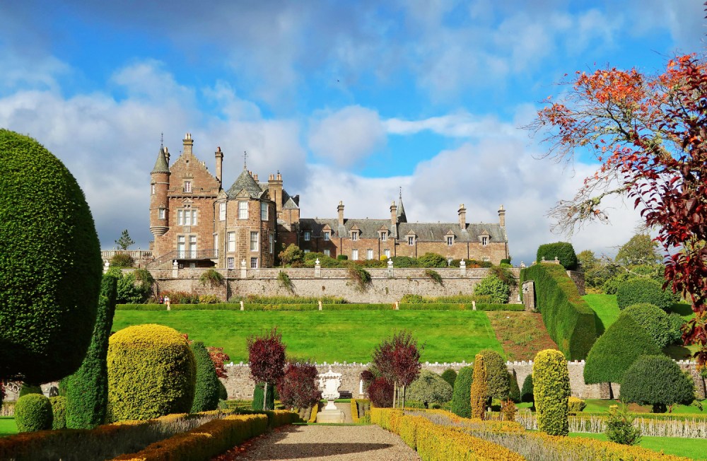 Historic mansion with manicured gardens, topiary, and clear blue sky.