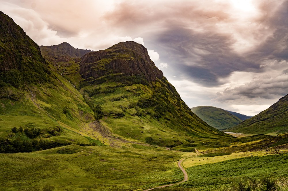 Lush green valley with steep mountains under a cloudy sky.