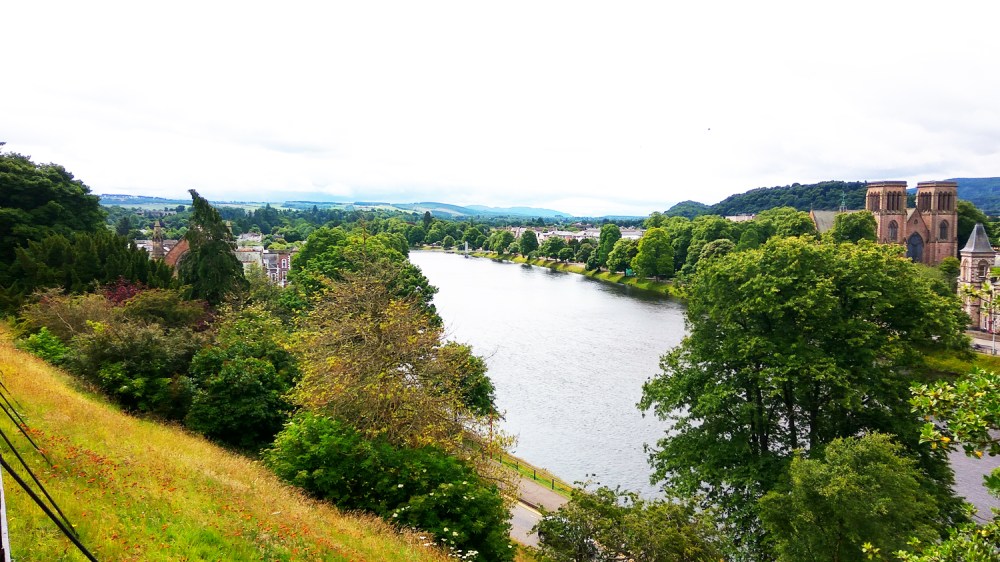 River flanked by trees with a distant cityscape and cloudy sky.
