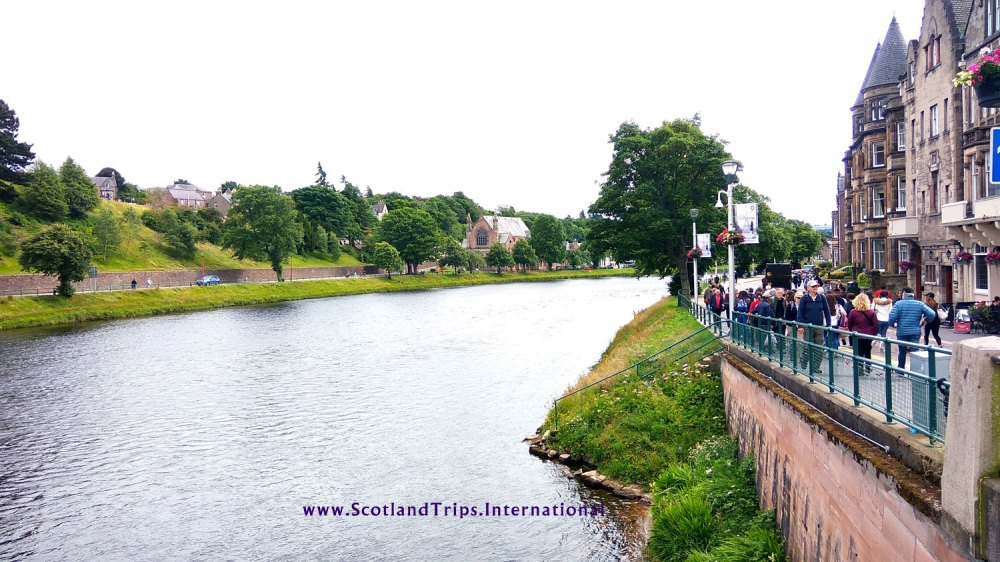 Río con árboles y edificios a ambos lados, gente caminando por un sendero.