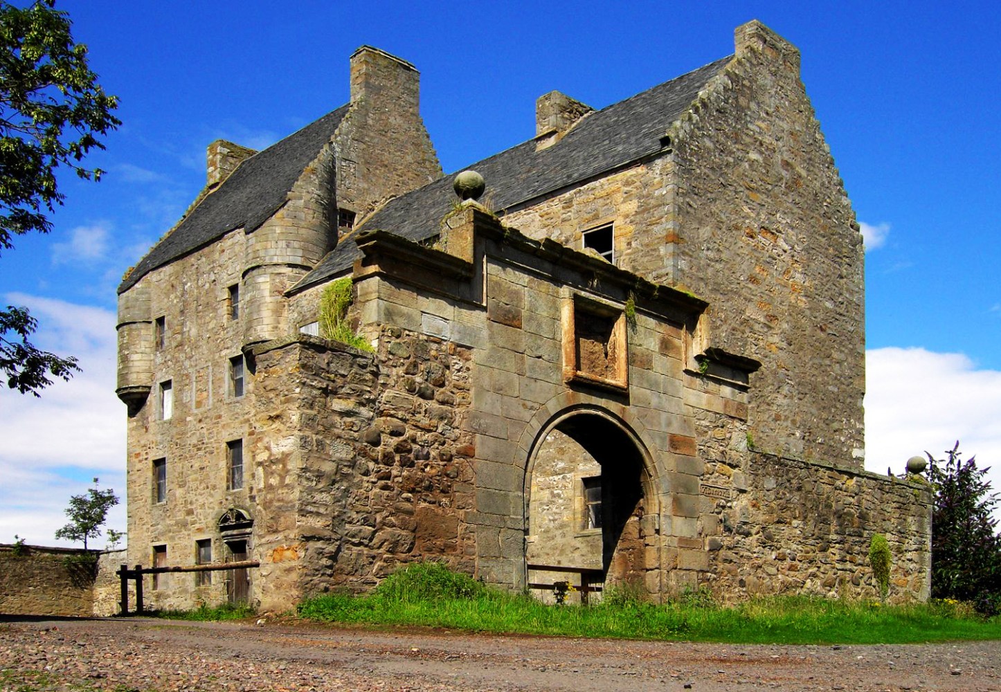 Historic stone castle with arched entrance and blue sky background.