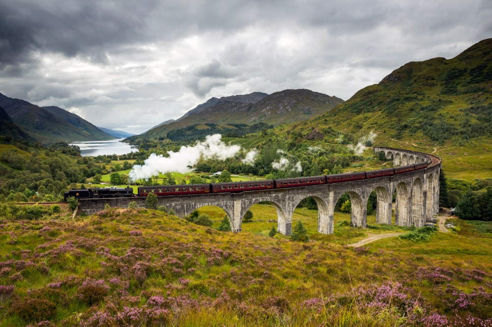 Tren cruzando un viaducto en un paisaje montañoso y exuberante bajo un cielo nublado.