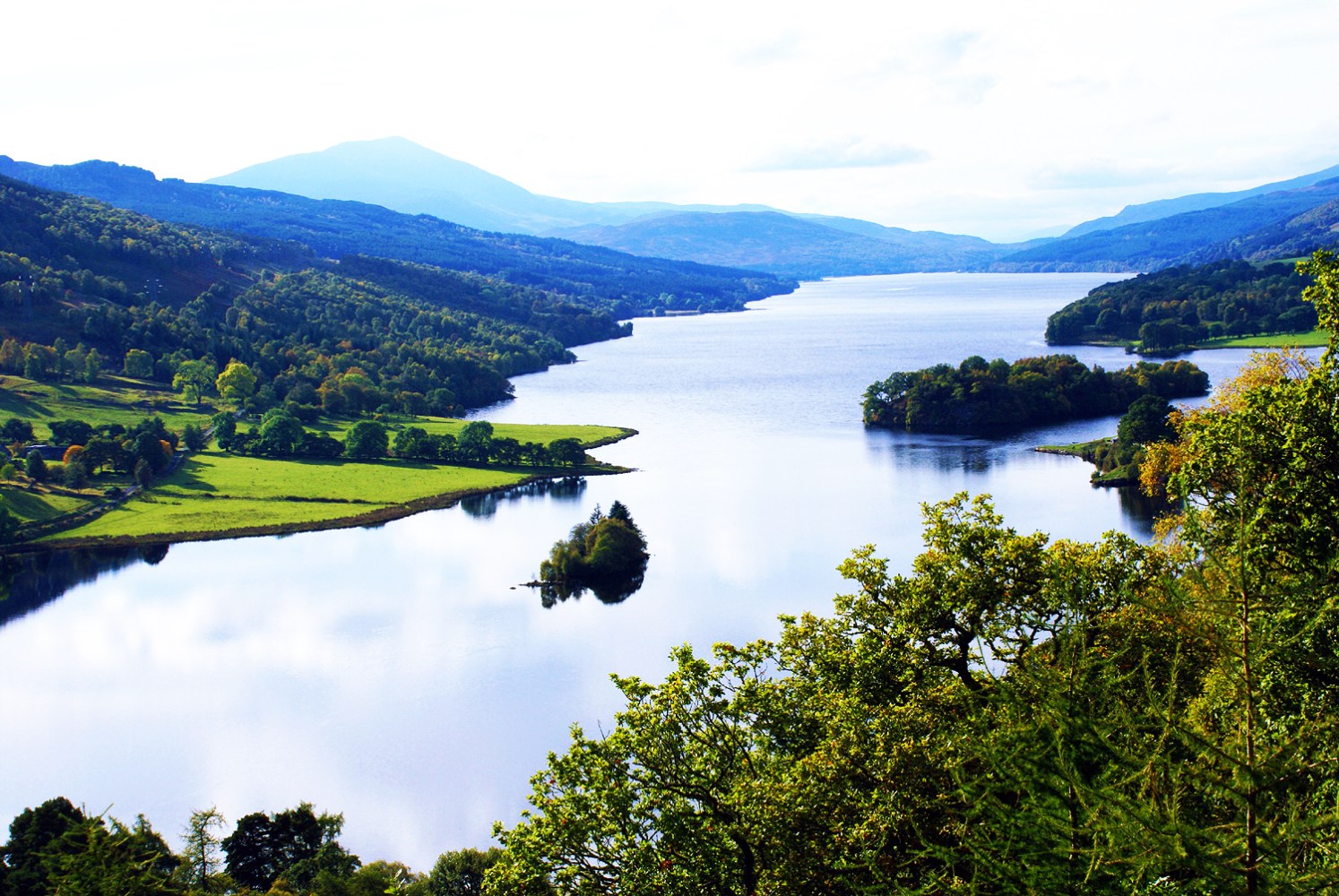 Scenic view of a winding river surrounded by lush green hills and trees under a clear sky.