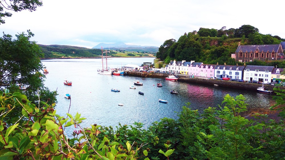 Colorful houses by a bay with boats and greenery in the foreground.