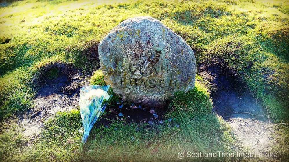 Stone with 'Clan Fraser' engraving and flowers on grassy ground.