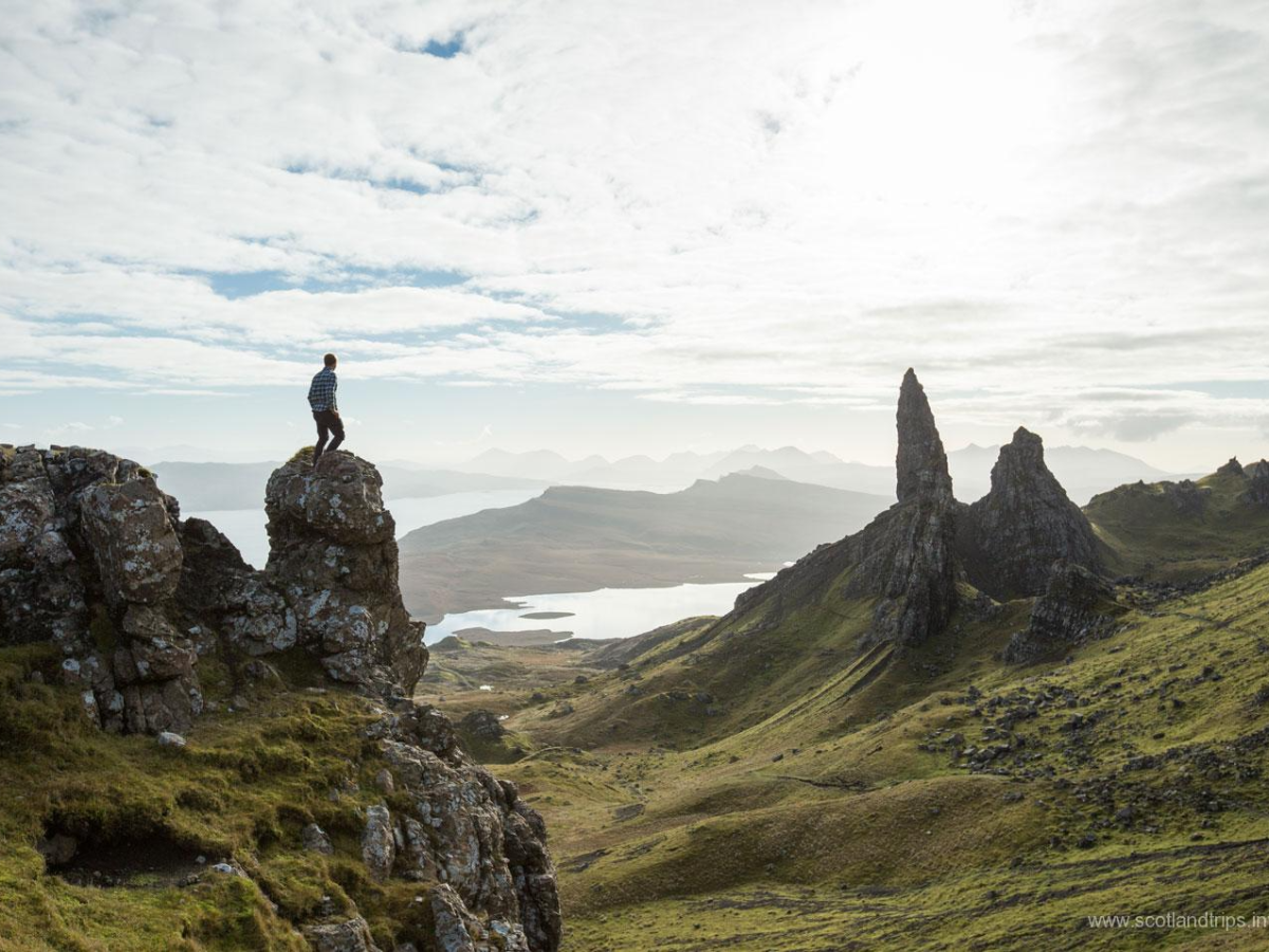 Person standing on a rocky cliff overlooking a dramatic landscape with a tall rock formation.
