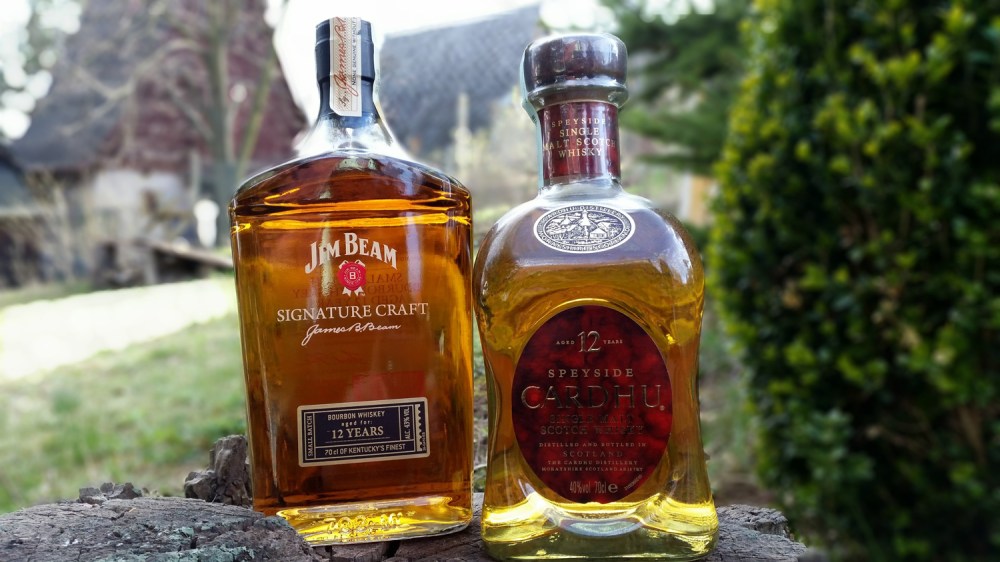 Two whiskey bottles on a stump outdoors with blurred background.